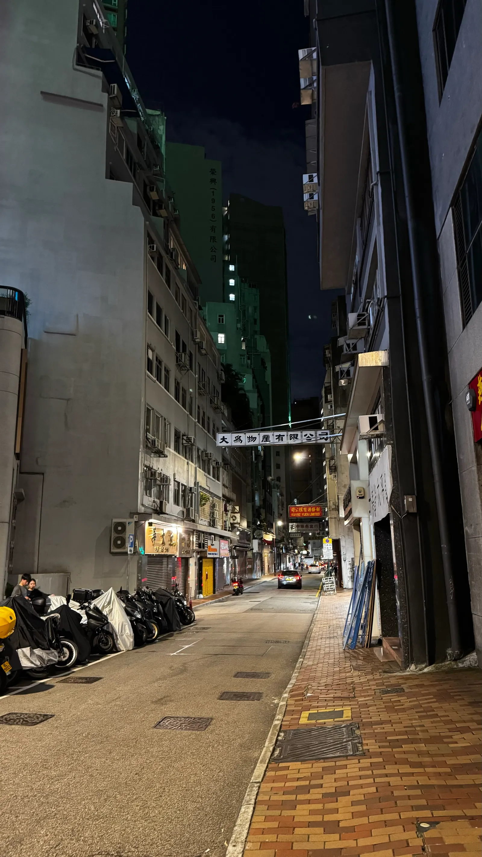 Une ruelle de Hong Kong la nuit, scooters alignés et enseignes